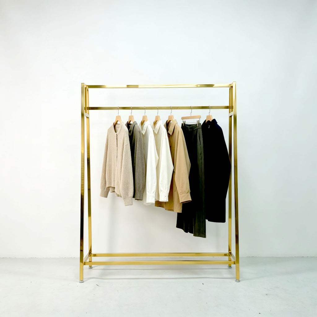 Modern gold clothing display rack holding sweaters, shirts, and trousers against a clean white wall