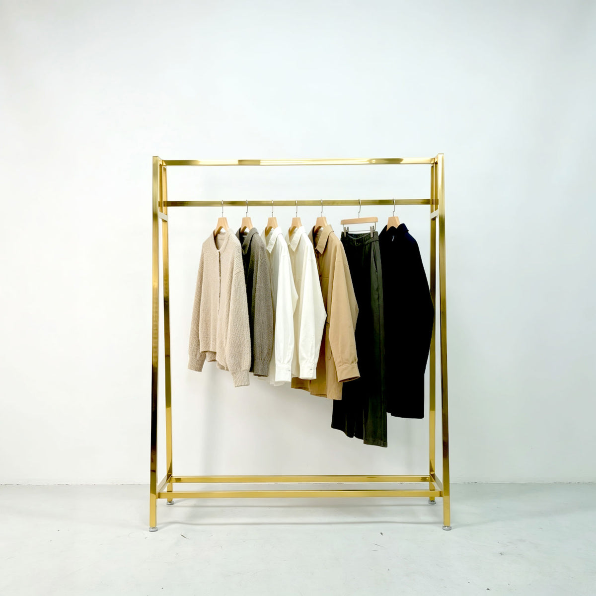 Modern gold clothing display rack holding sweaters, shirts, and trousers against a clean white wall